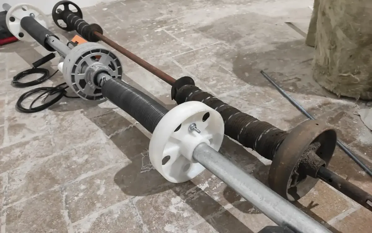 Eje con motor tubular nuevo junto al eje viejo con muelles y poleas desgastadas