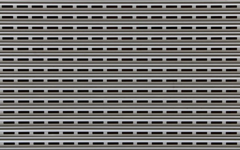 Contactanos Close-up view of a textured metallic roll-up door showcasing repetitive horizontal patterns.