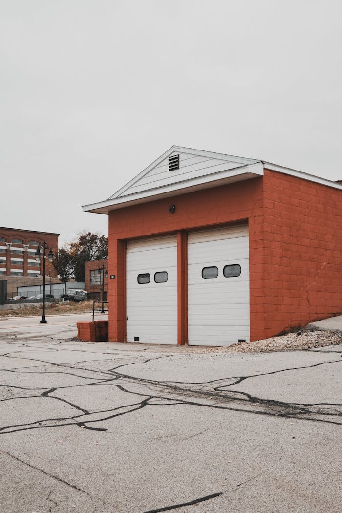 Urban scene capturing a red-brick garage building with double doors, set on a quiet street.